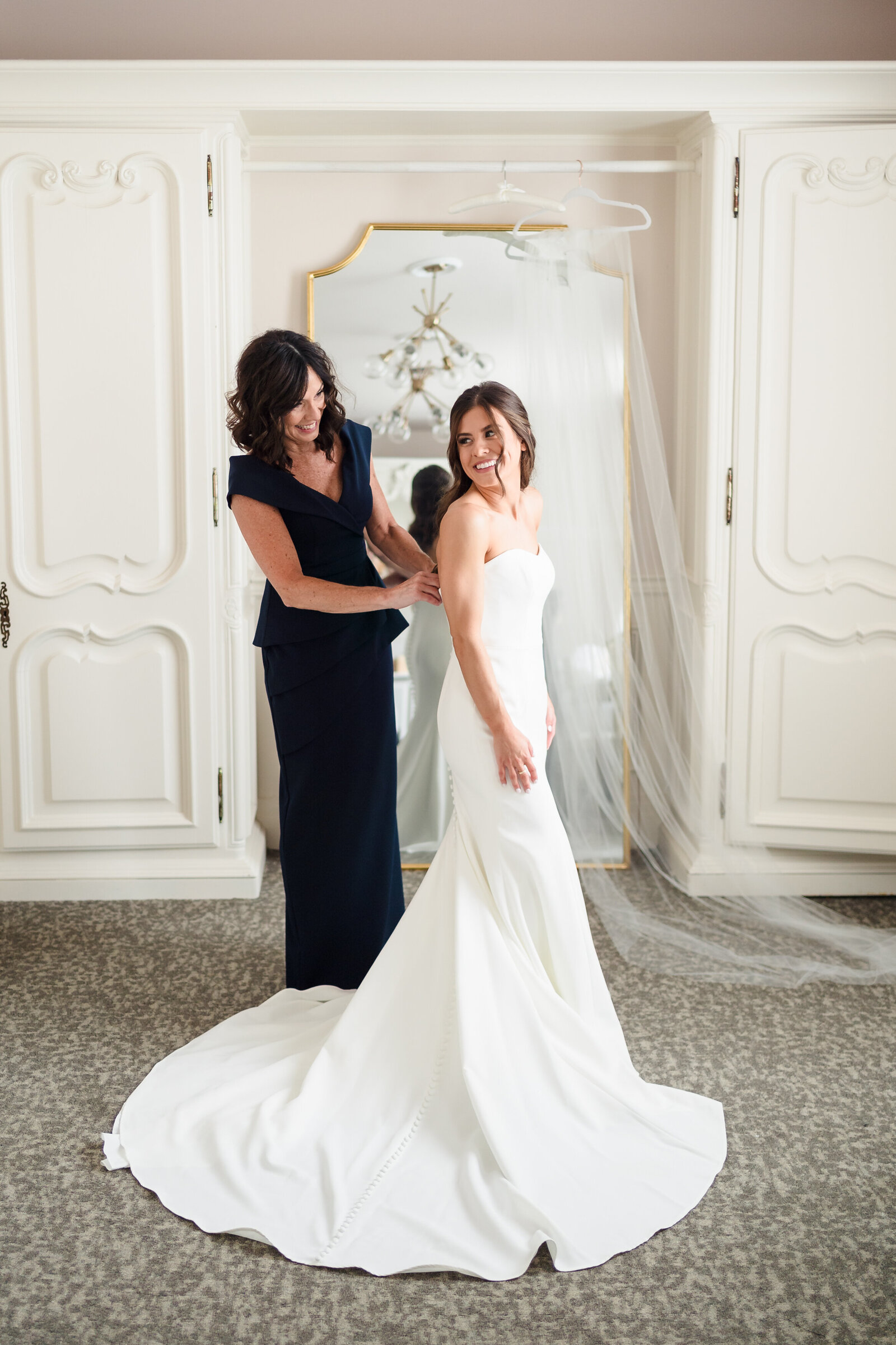 The mother of the bride helps her daughter button her wedding dress inside the bride's suite at Pinnacle Golf Club