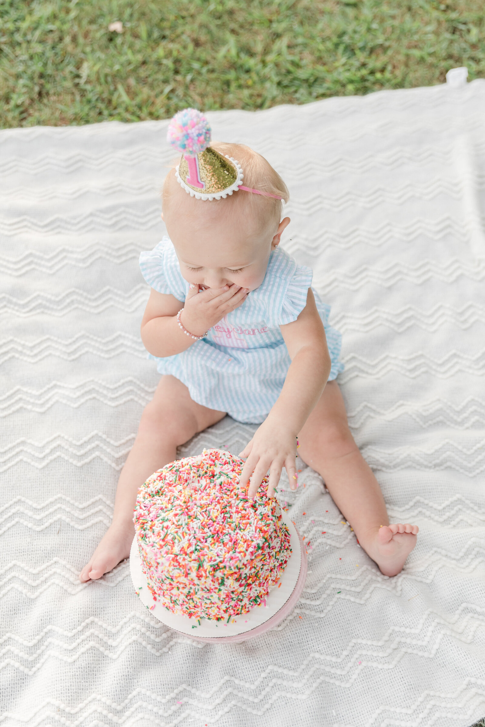 Baby digging into a sprinkled covered first birthday cake.