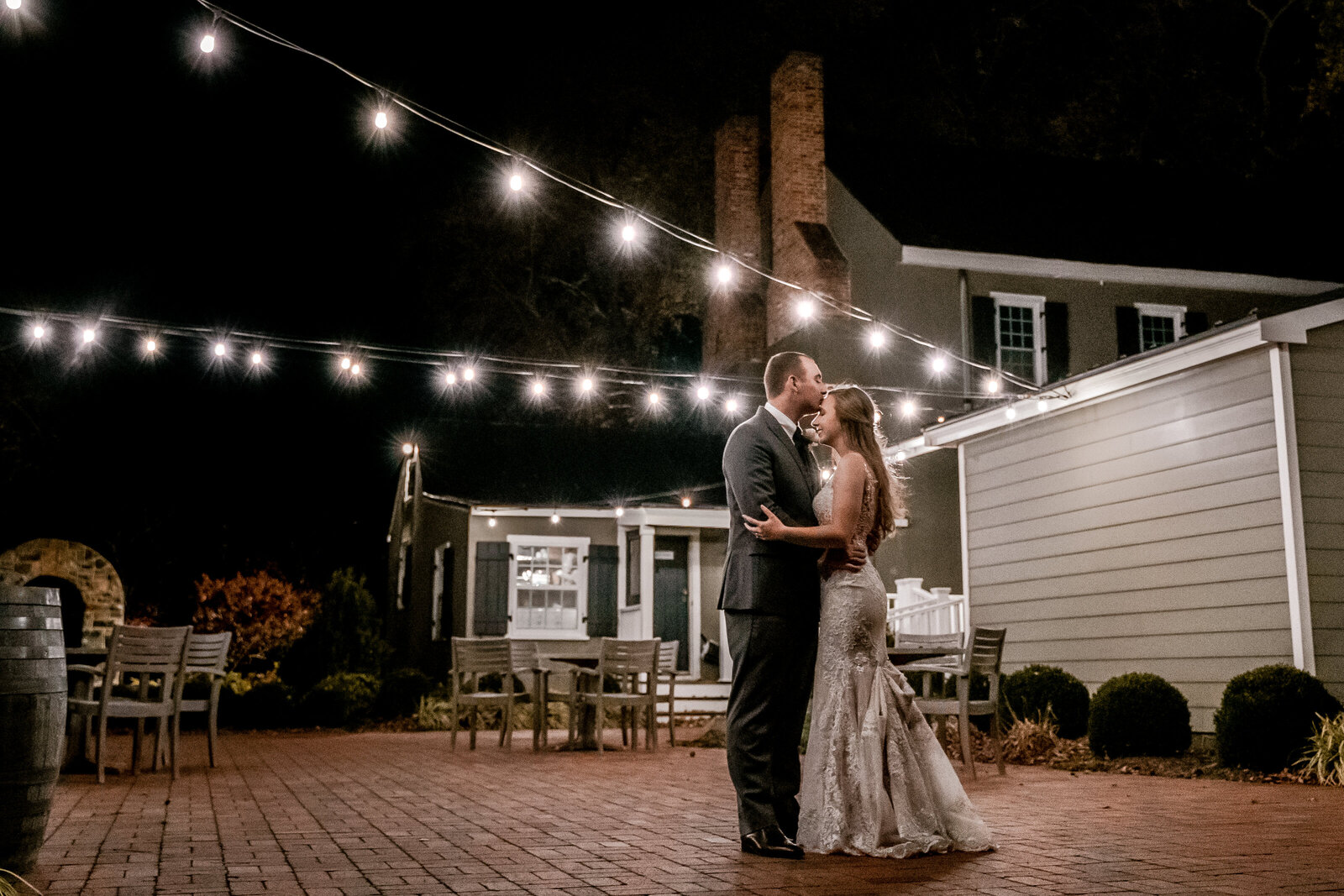 A bride and groom share a dance under string lights on a patio during their wedding at Fleetwood Farm Winery in Leesburg Virginia