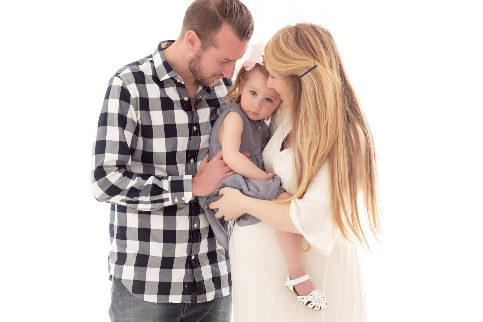 Maternity photo of a pregnant mom standing with her husband and young daughter, lovingly holding her baby bump