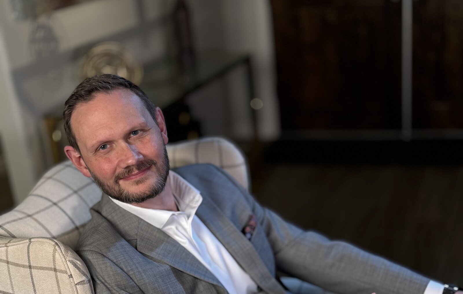 Confident middle-aged man in a light gray suit smiling warmly, representing a professional Peace Coach offering spiritual and practical guidance. Ideal for personal growth, emotional resilience, and finding peace