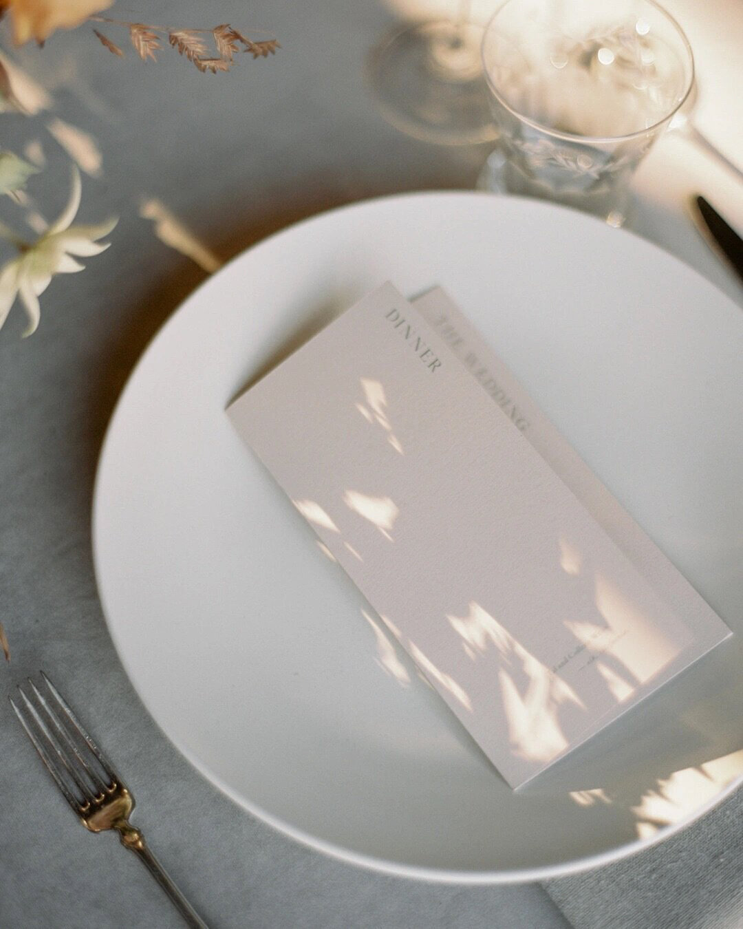 Minimalist wedding table details  with shadows of flowers falling on light pink menu on top of light blue velvet linens 