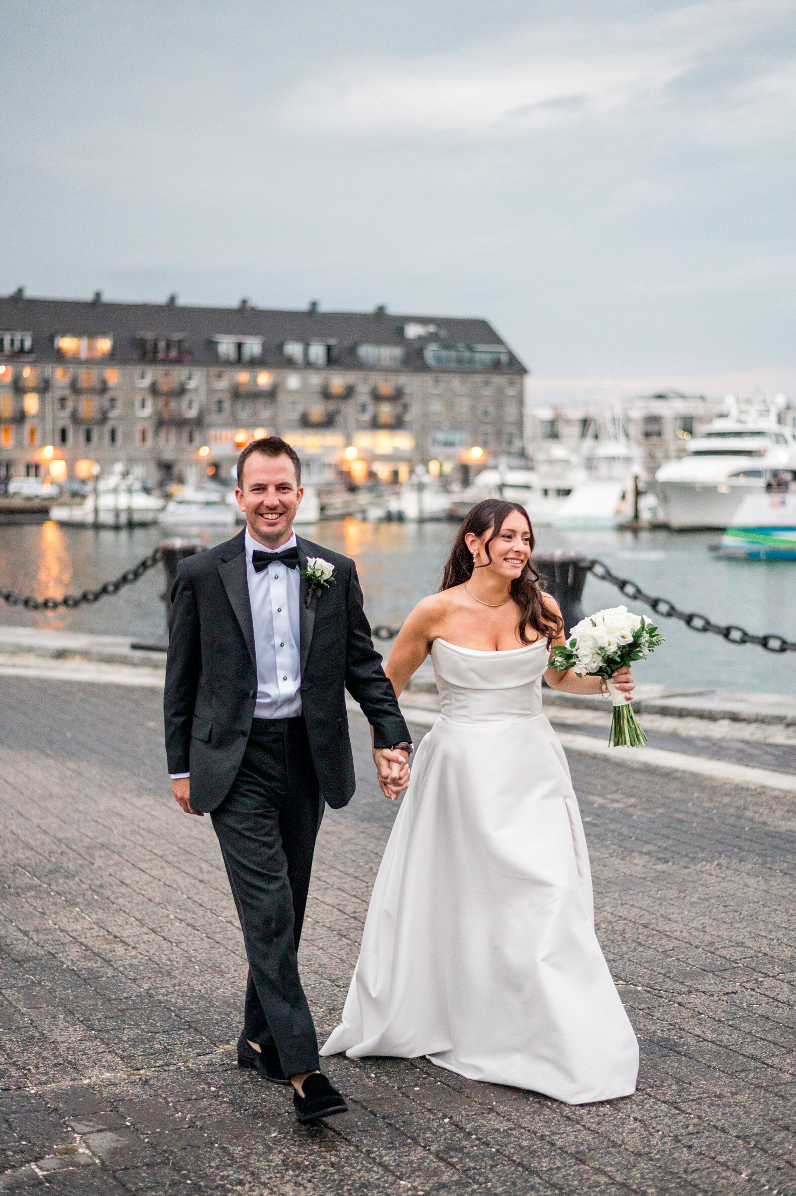Bride and groom walking along Boston Harbor at sunset during elegant Boston wedding at the Marriott Long Wharf — romantic luxury photography by Sarah Surette Photography.