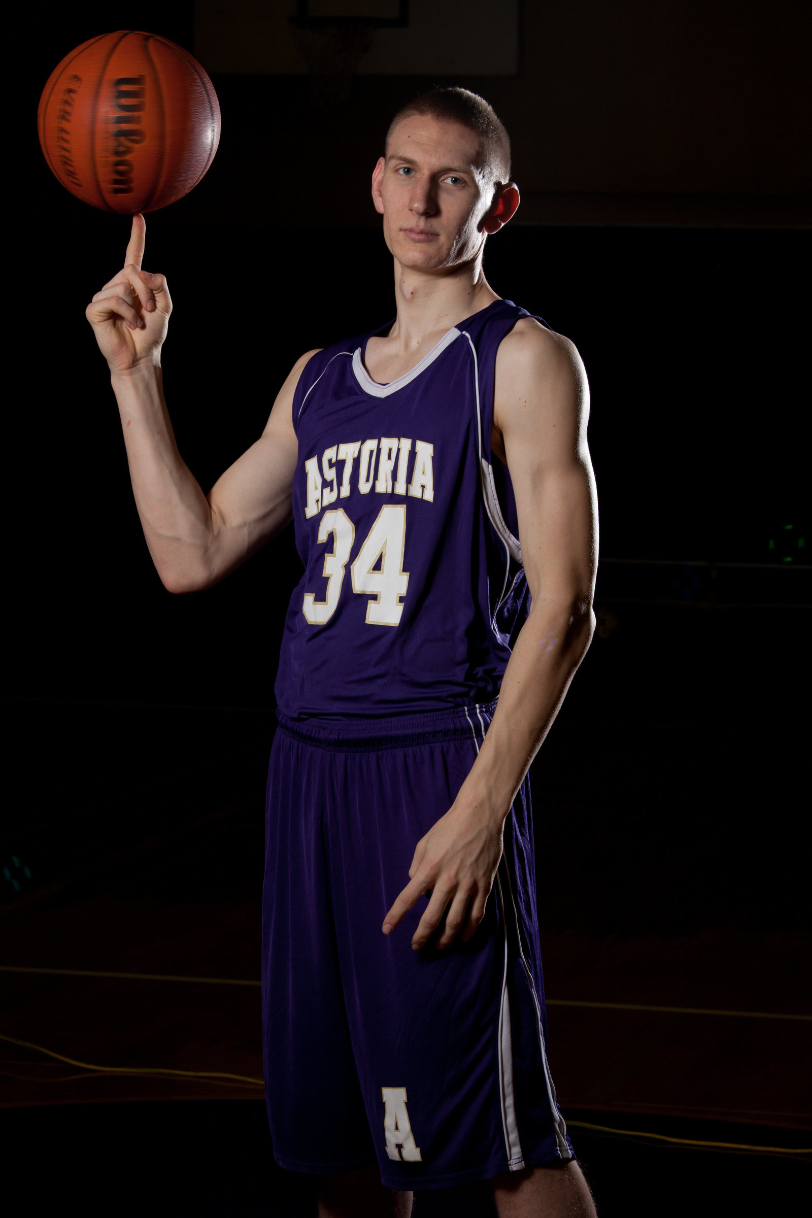 A graduate of Astoria high school Spins a basketball on one finger in the Astoria Oregon high school gym. He has the purple Astoria uniform on.