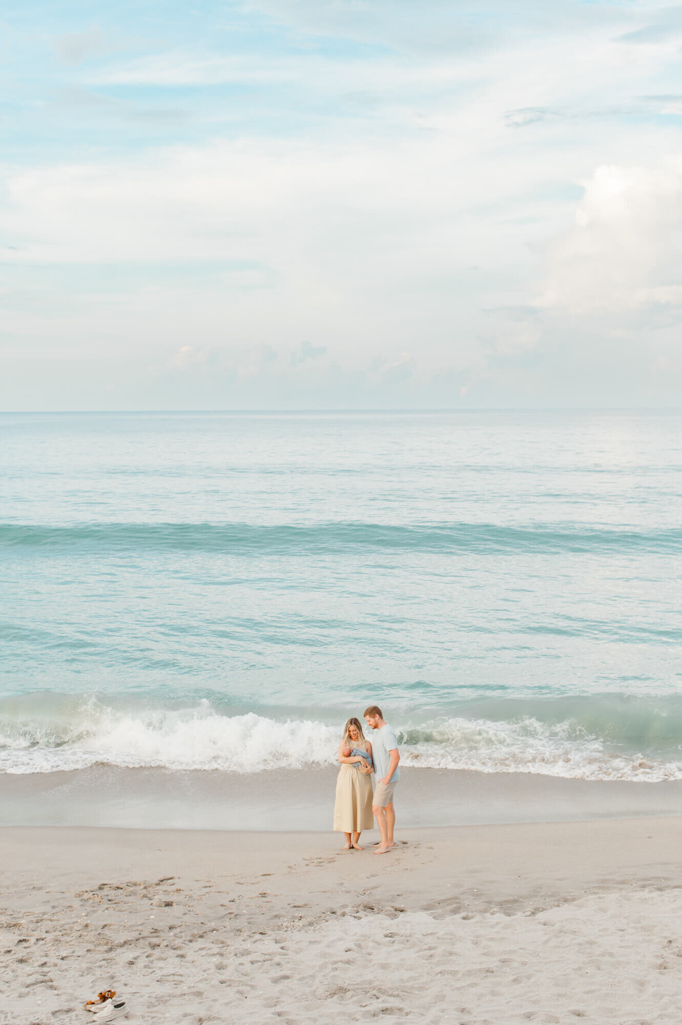 Stunning image of beautiful Vero Beach with parents standing down by the shoreline holding their newborn baby boy!