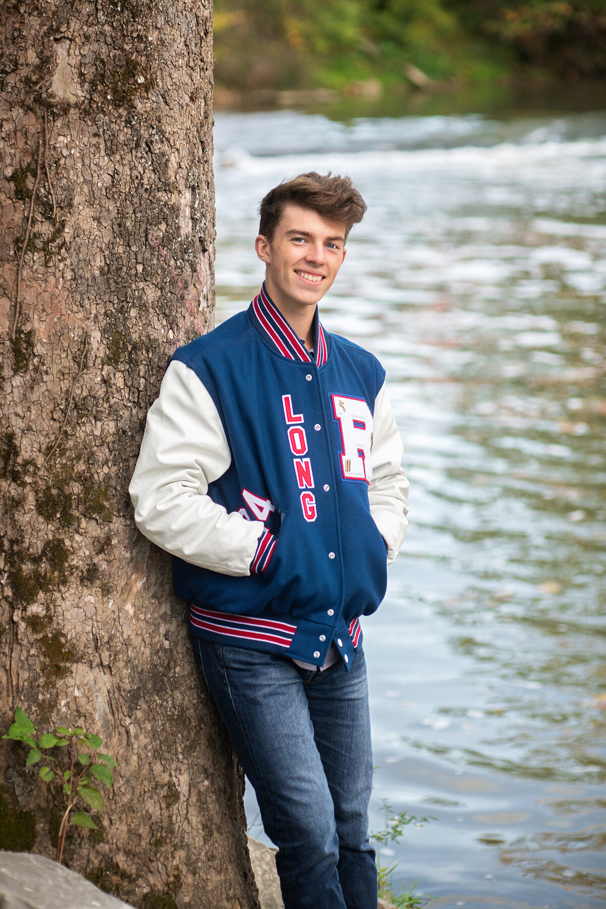 boy wearing revere high school varsity jacket smiles by the water  at lock 29 trailhead