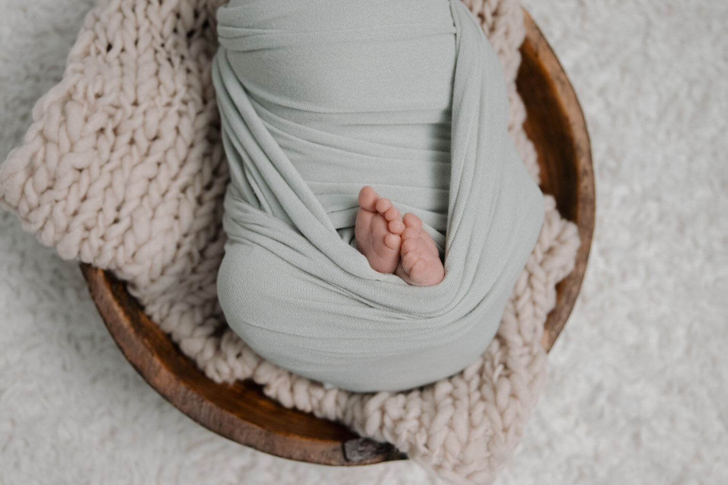 Tiny newborn baby feet peeking out from a green wrap, laying on a knitted blanket