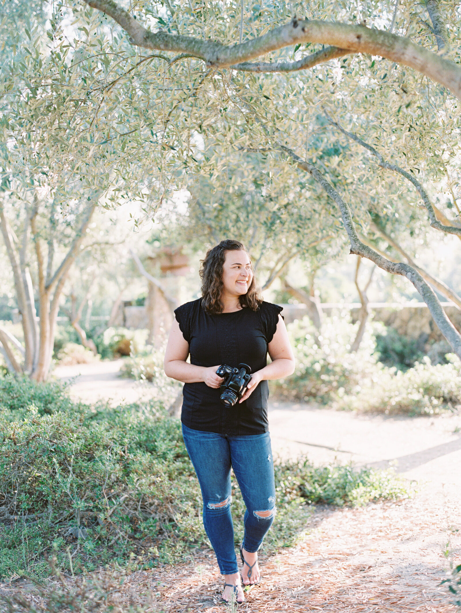 Woman walking along a path while holding a camera.