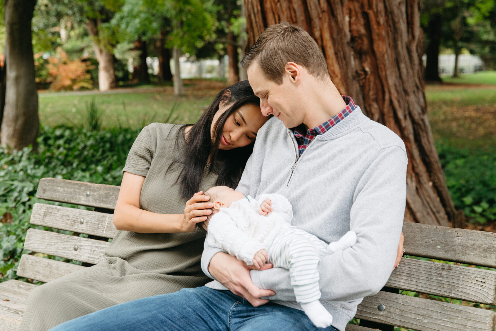 new parents sitting on a park bench and smiling down at their newborn daughter