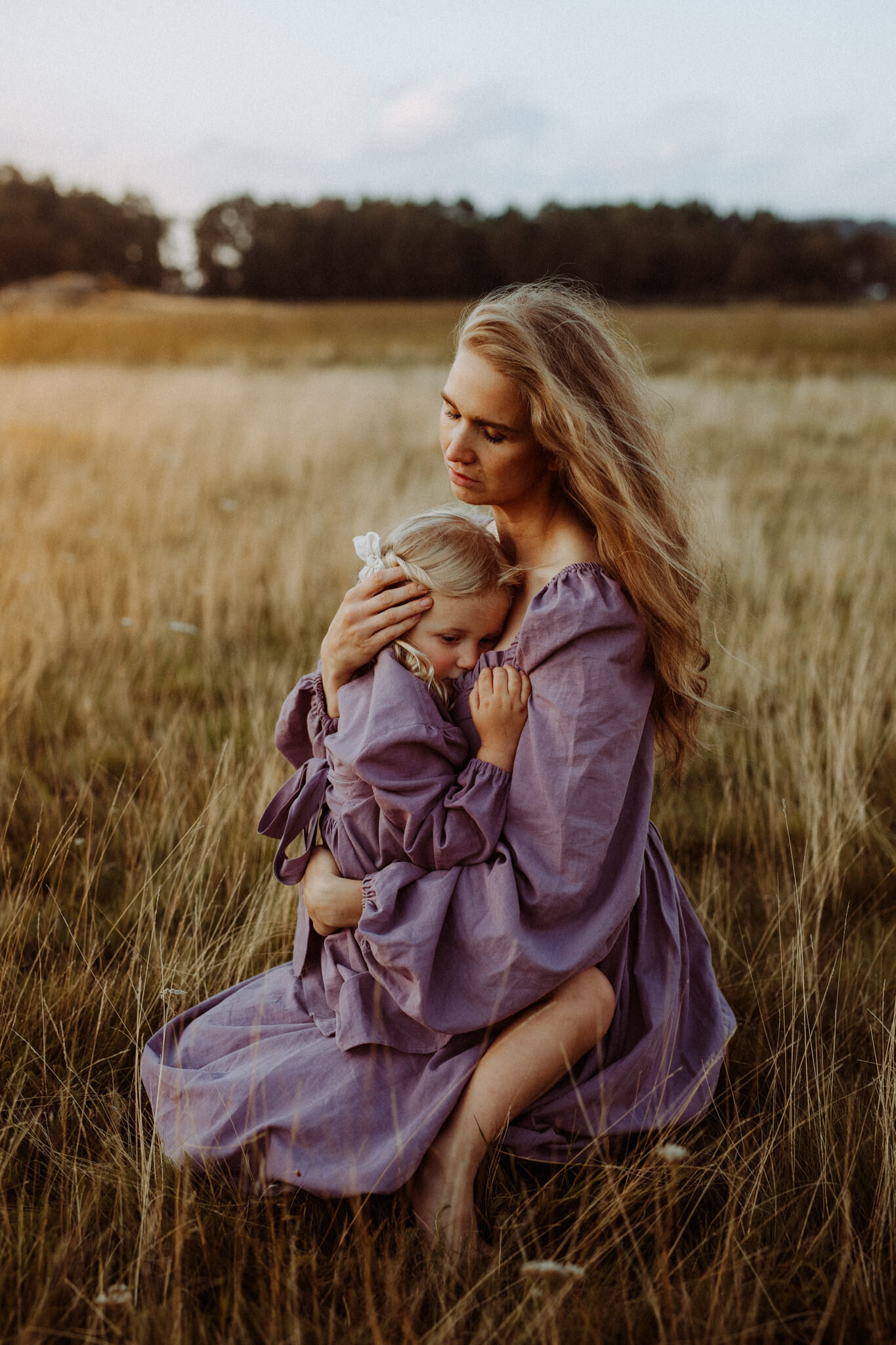en mamma och hennes dotter sitter i lila klänningar på ett fält