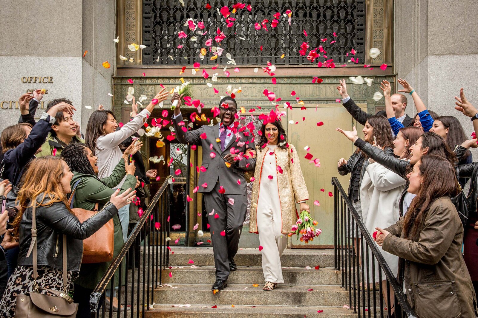 Wedding guests throwing rose petals as a wedding couple walks down a staircase.