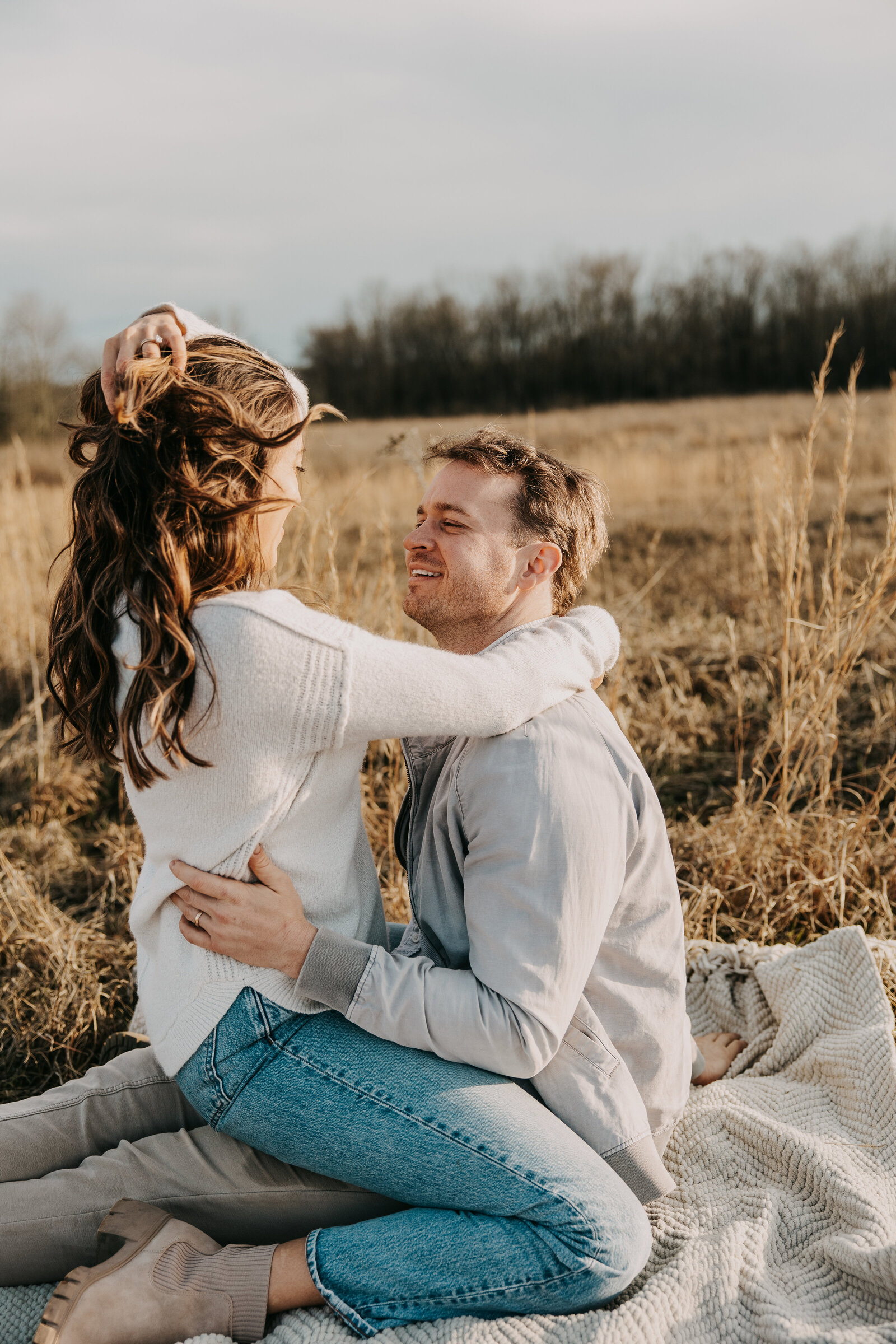 Kelly and Jordan on a blanket in a field, Kelly in Jordan's lap, his hands on her waist, hers around his shoulders.