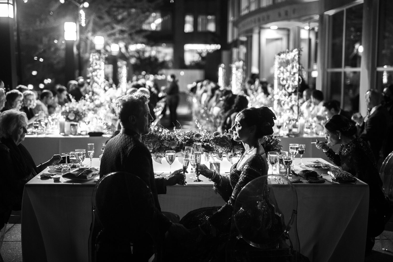 A man and a woman are sitting at a long table with glasses of wine.