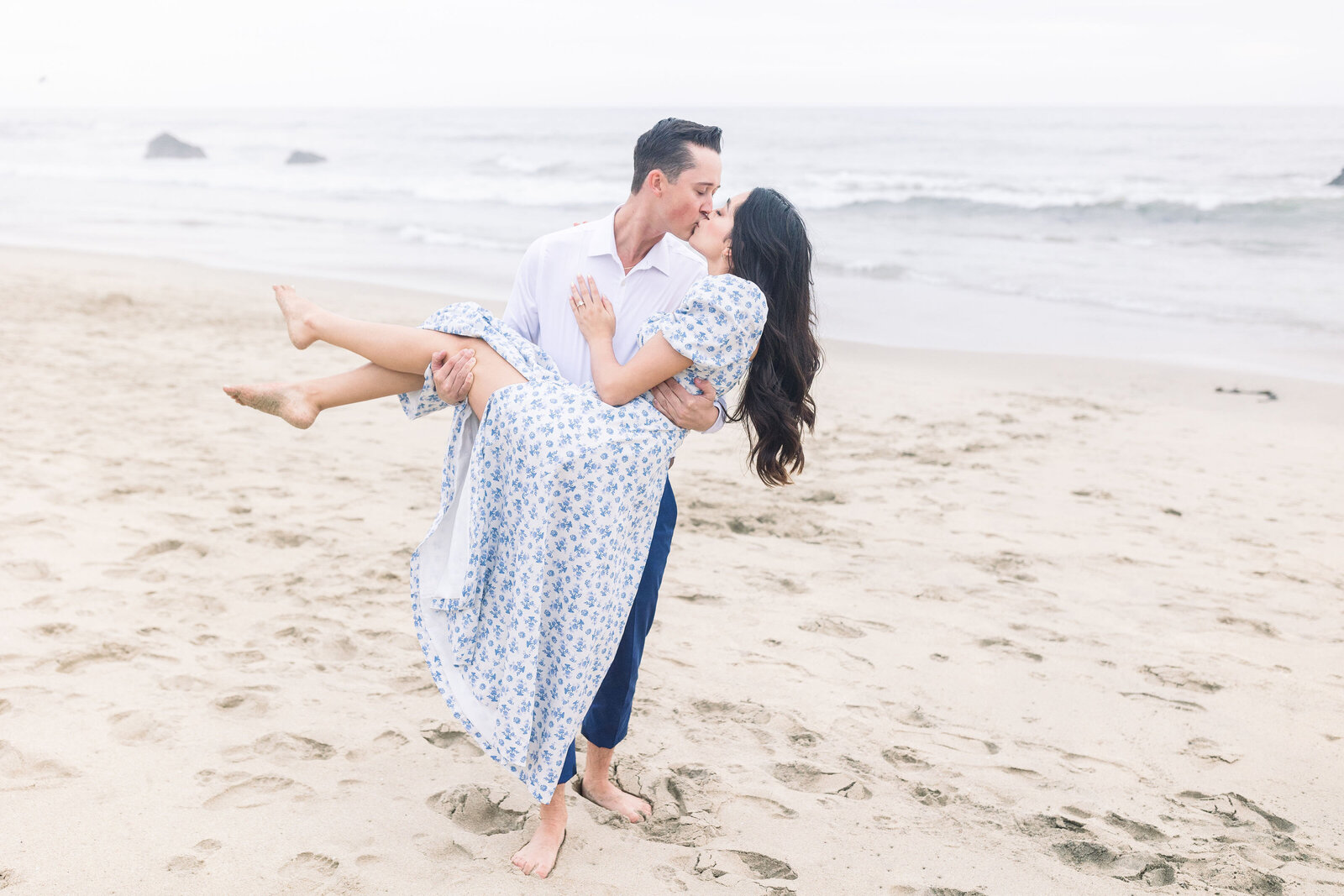 man carrying his fiance on the beach at Half Moon Bay for beach engagement photos by wedding photographer bay area