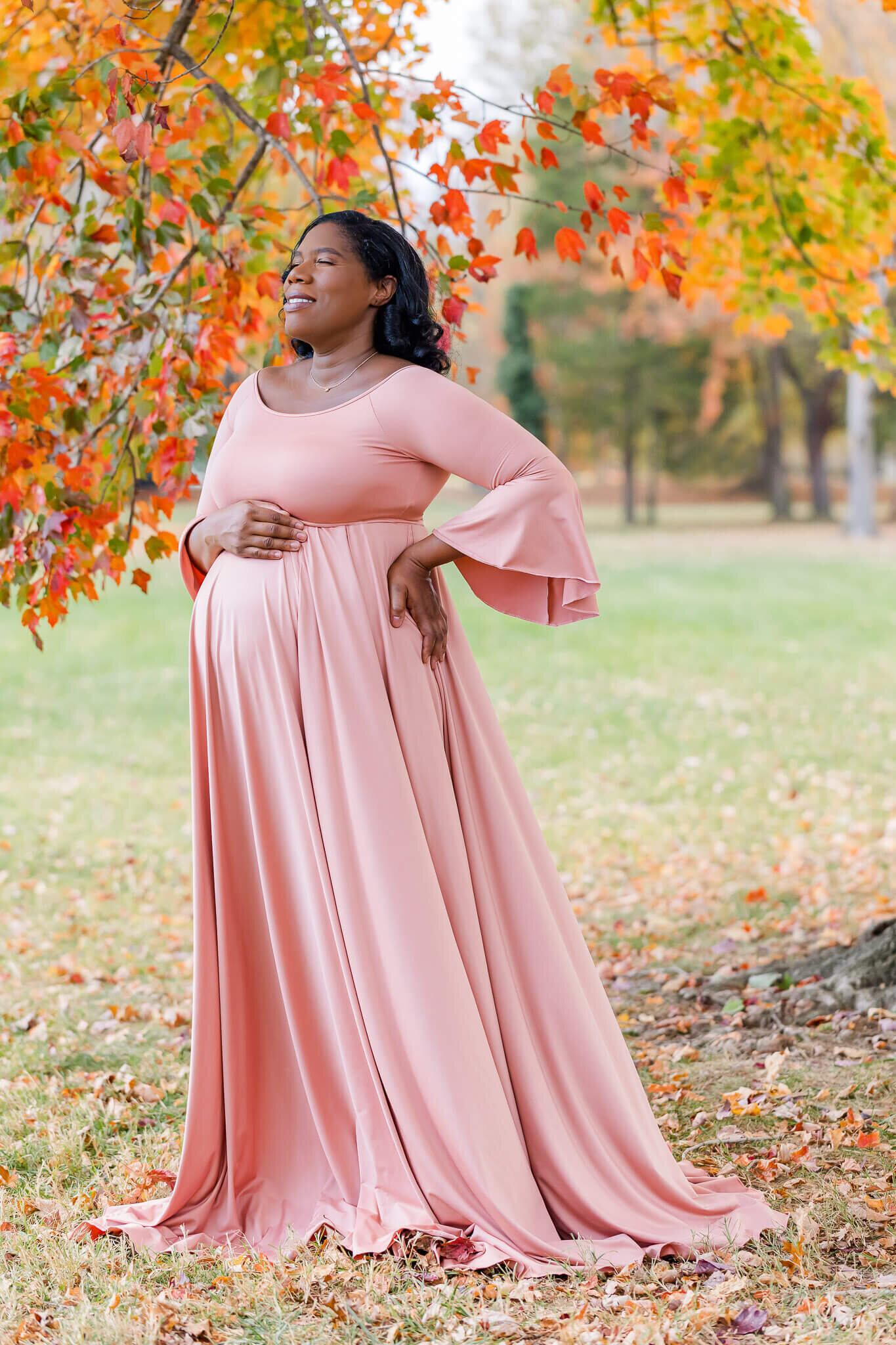 A beautiful pregnant woman in a pink dress posing for her maternity portraits in an Alexandria, Virginia park.