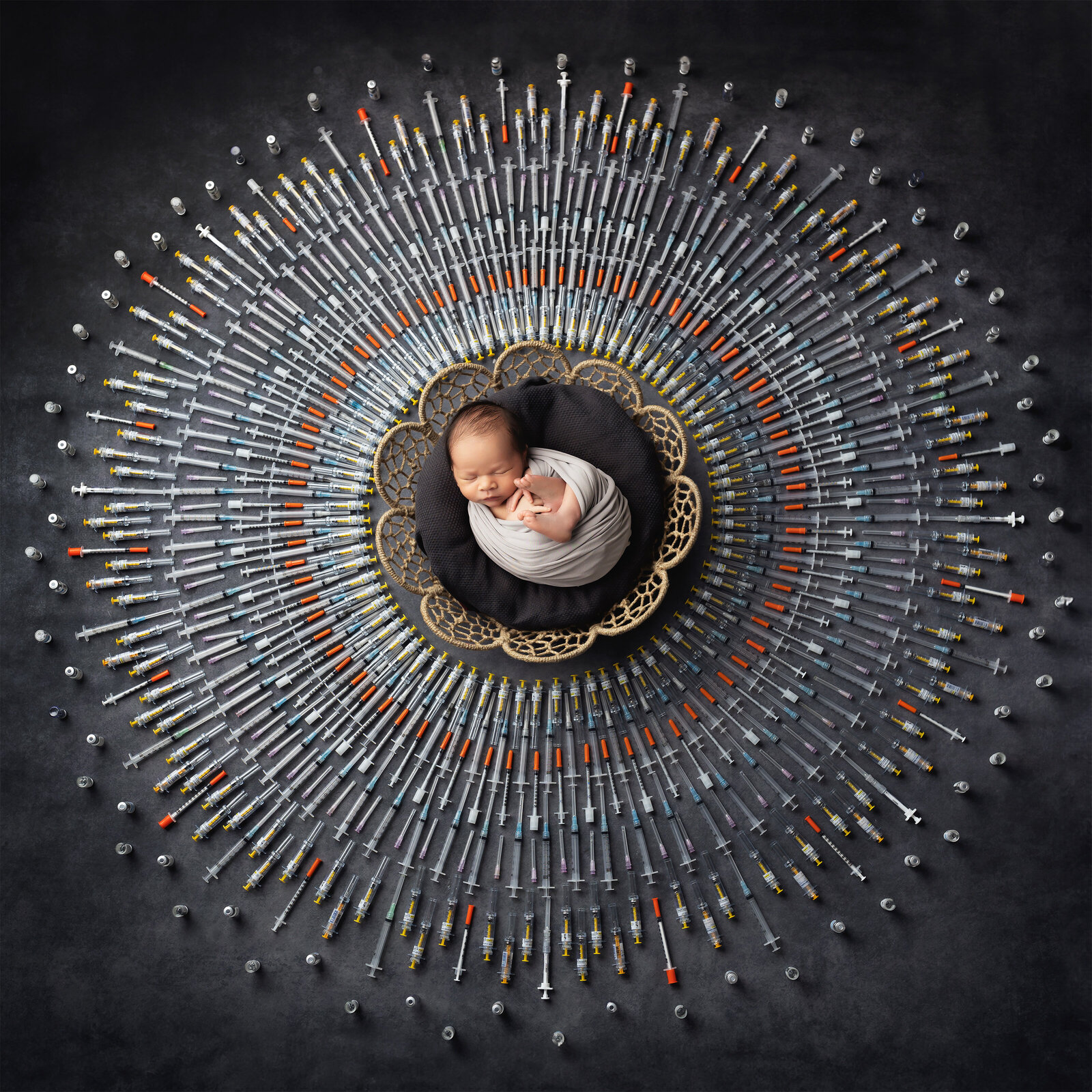 Newborn baby swaddled in gray and sleeping peacefully inside a basket, surrounded by syringes and vials representing the IVF journey. A powerful image honoring infertility warriors created by an IVF photographer.