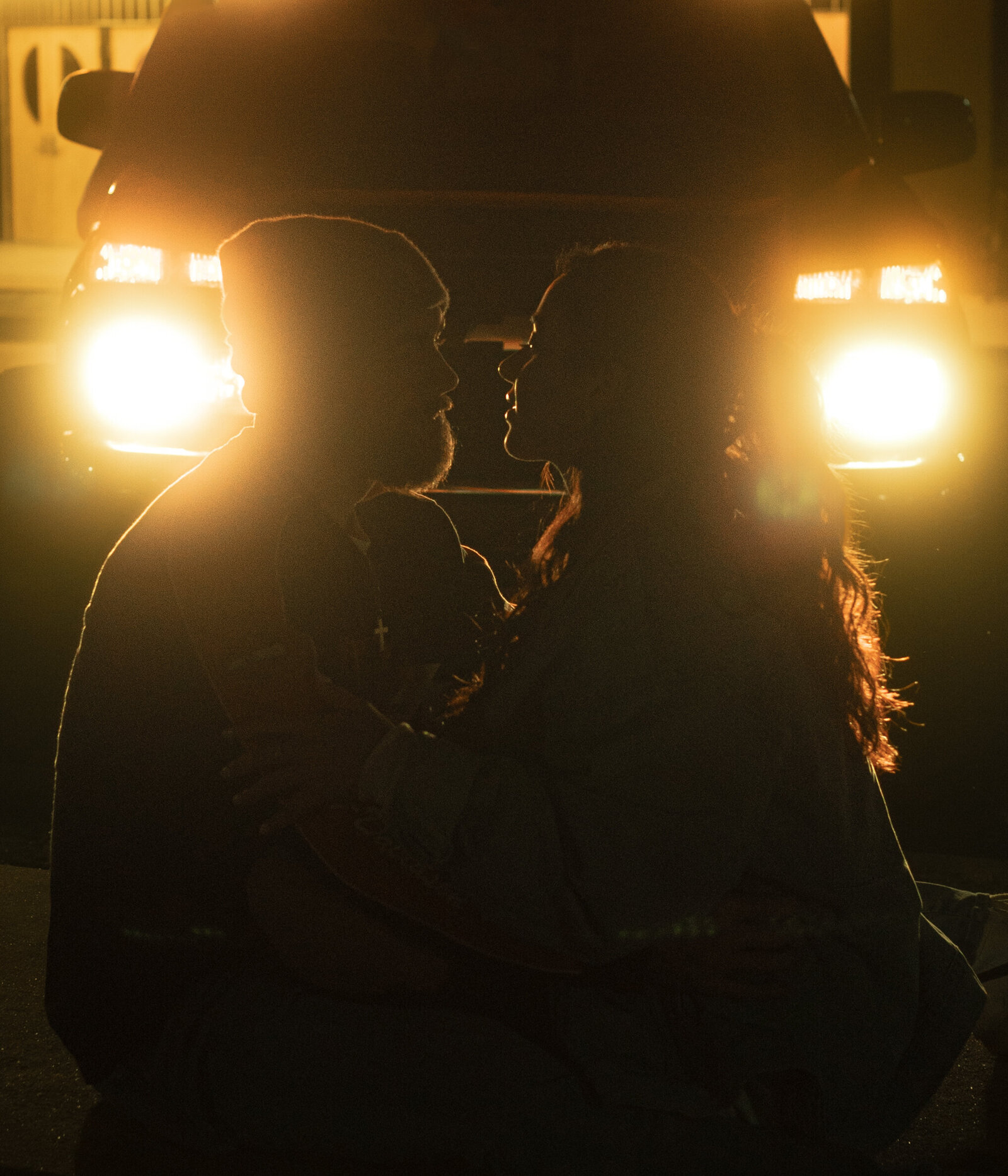A couple snuggling on a cold Tennessee night leaning in for a kiss in front of their truck headlights captured in a documentary style.