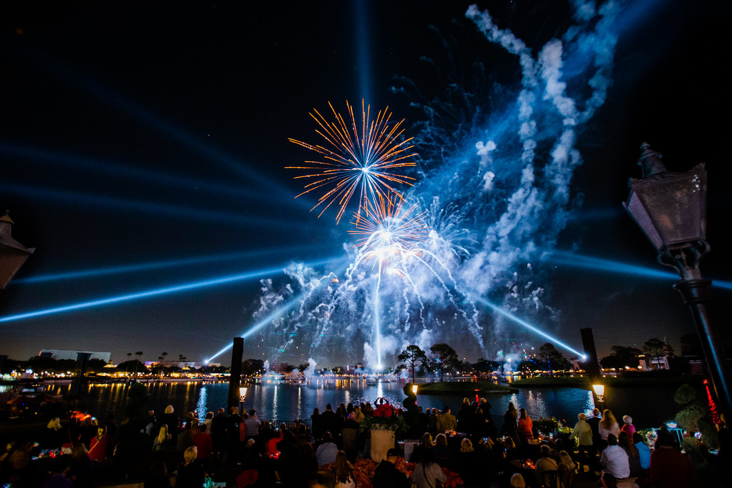 Fireworks and laser show in the sky over a crowd and lake at EPCOT Disney