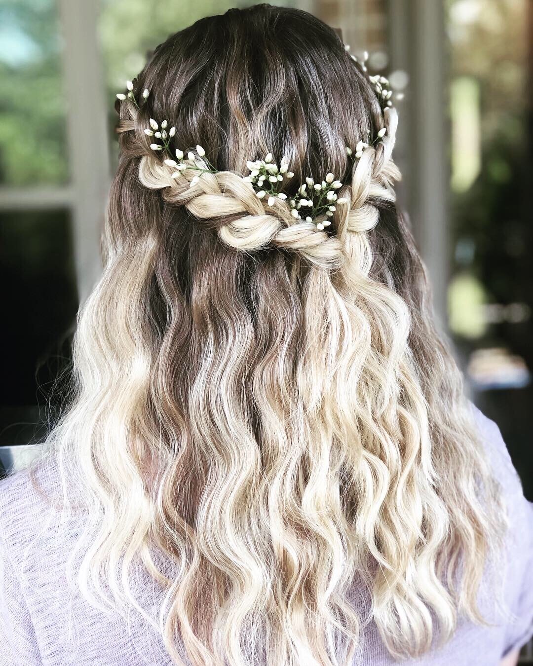 Blonde hair with a braided crown adorned with small white flowers flows in gentle waves down the back, capturing the essence of a bridal beauty experience in Texas.