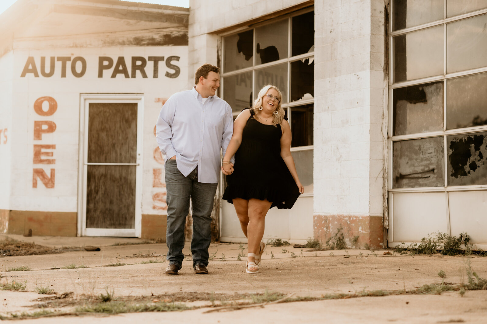 little rock ar downtown engagement session with man and woman holding hands and walking down the sidewalk together while laughing as the sunsets behind the buildings