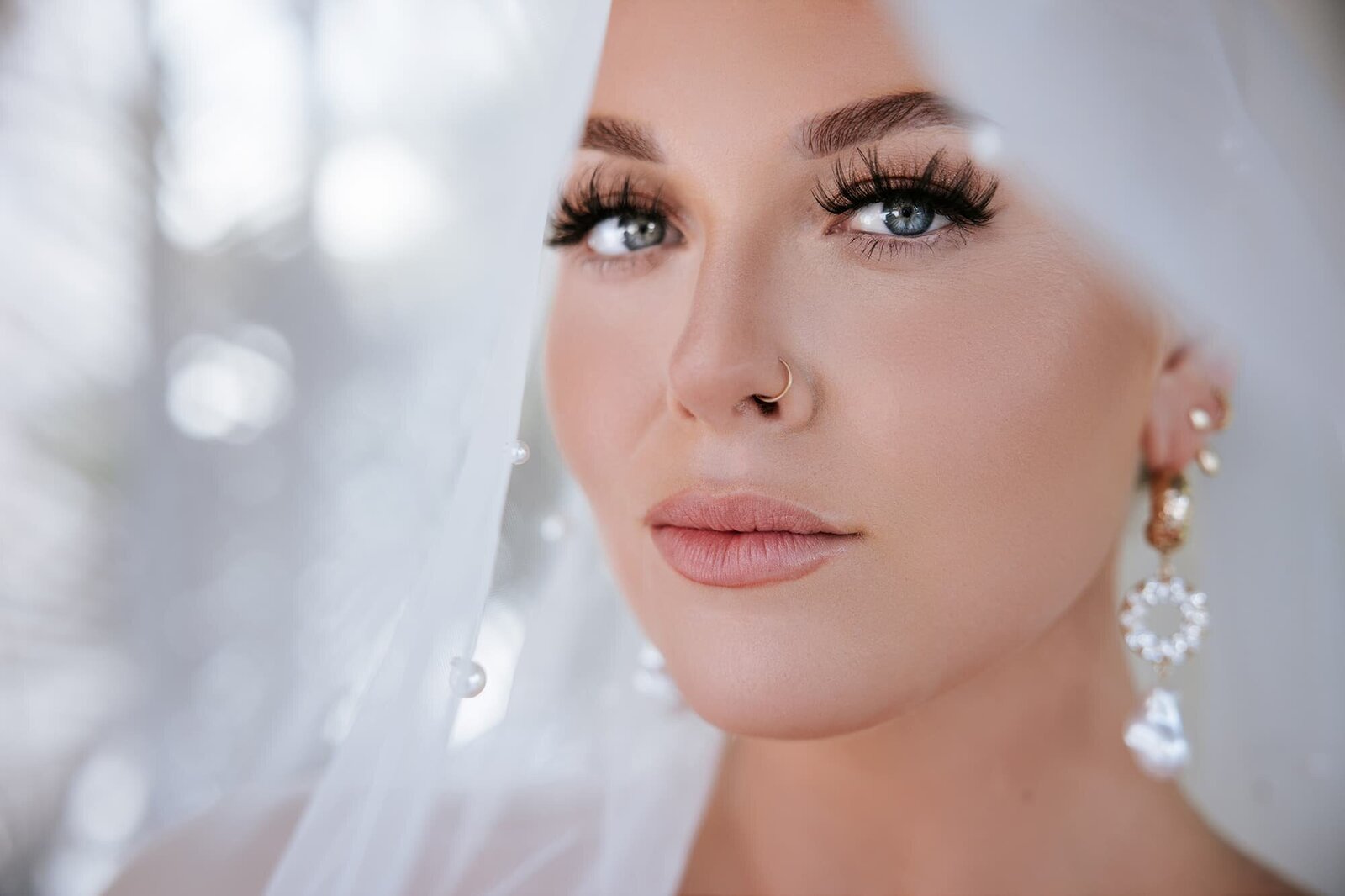 Close-up bridal portrait taken at Dreams Vallarta Bay Resort in Puerto Vallarta, Mexico, featuring a stunning bride with dramatic lashes, pearl-detailed veil, statement earrings, and a gold nose ring, captured by destination wedding photographer Logrono & Co.