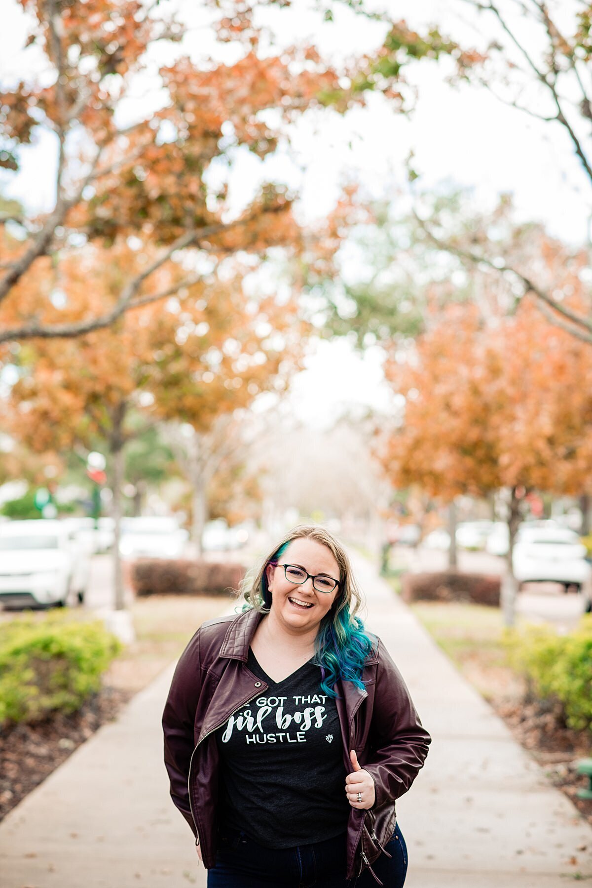 Mahlia smiling at camera wearing a dark purple leather jacket and girl boss shirt