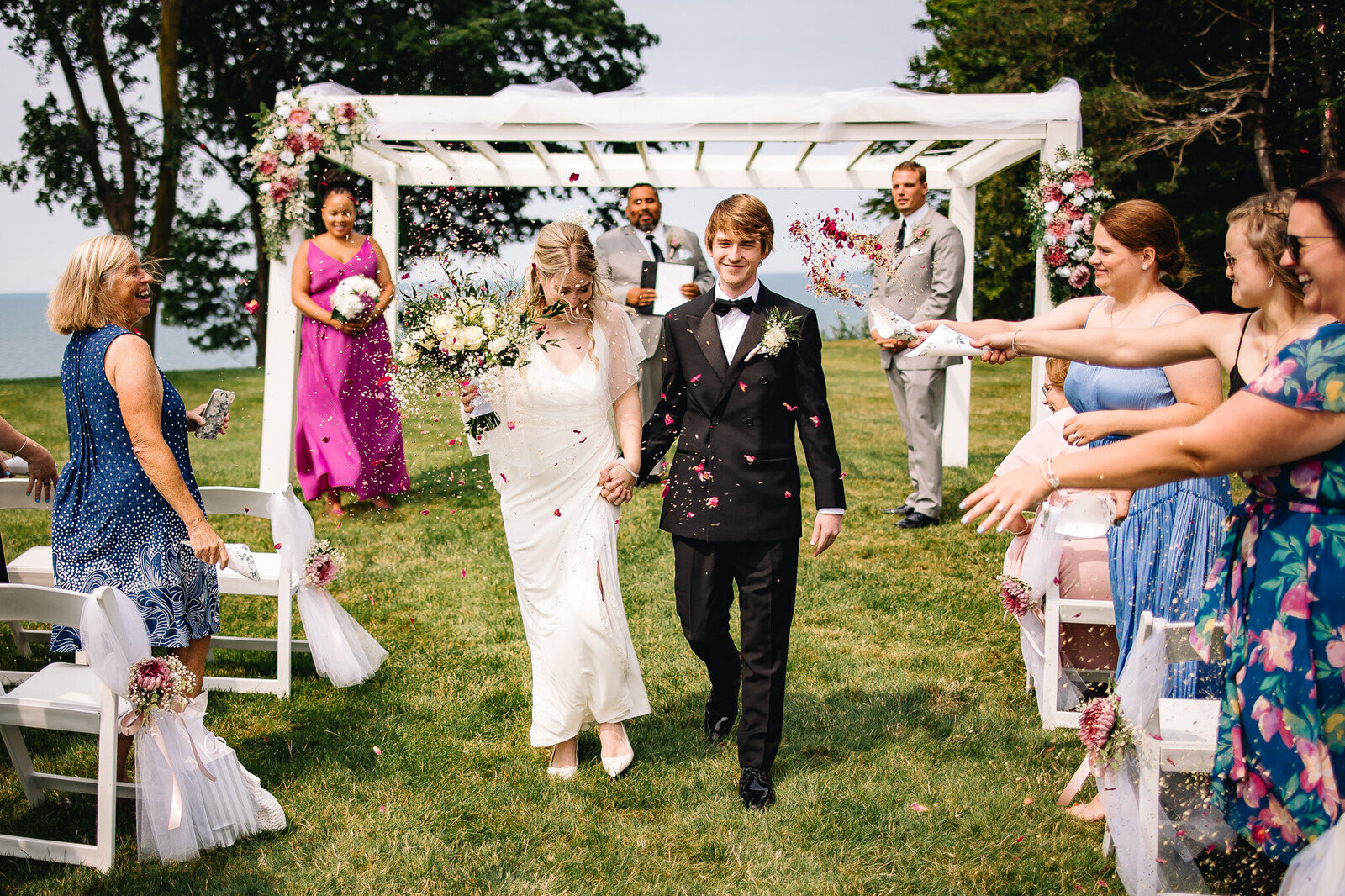 A bride and groom exit their wedding ceremony. Guests throwing dried flower petals over them as they walk.
