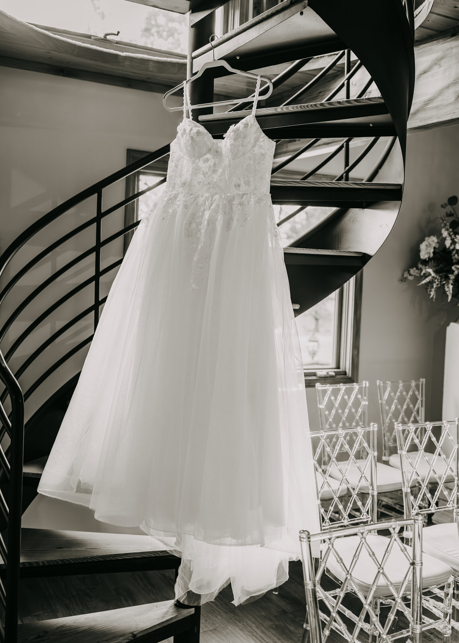 Black and white shot of bride's dress hanging from the spiral staircase in the ceremony room at Kincaid Manor, adding elegance.