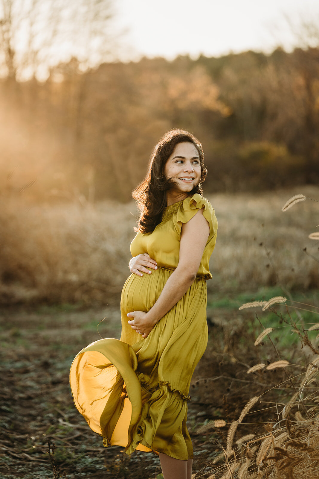 pregnant woman in yellow dress blows in wind during winter maternity session in boston