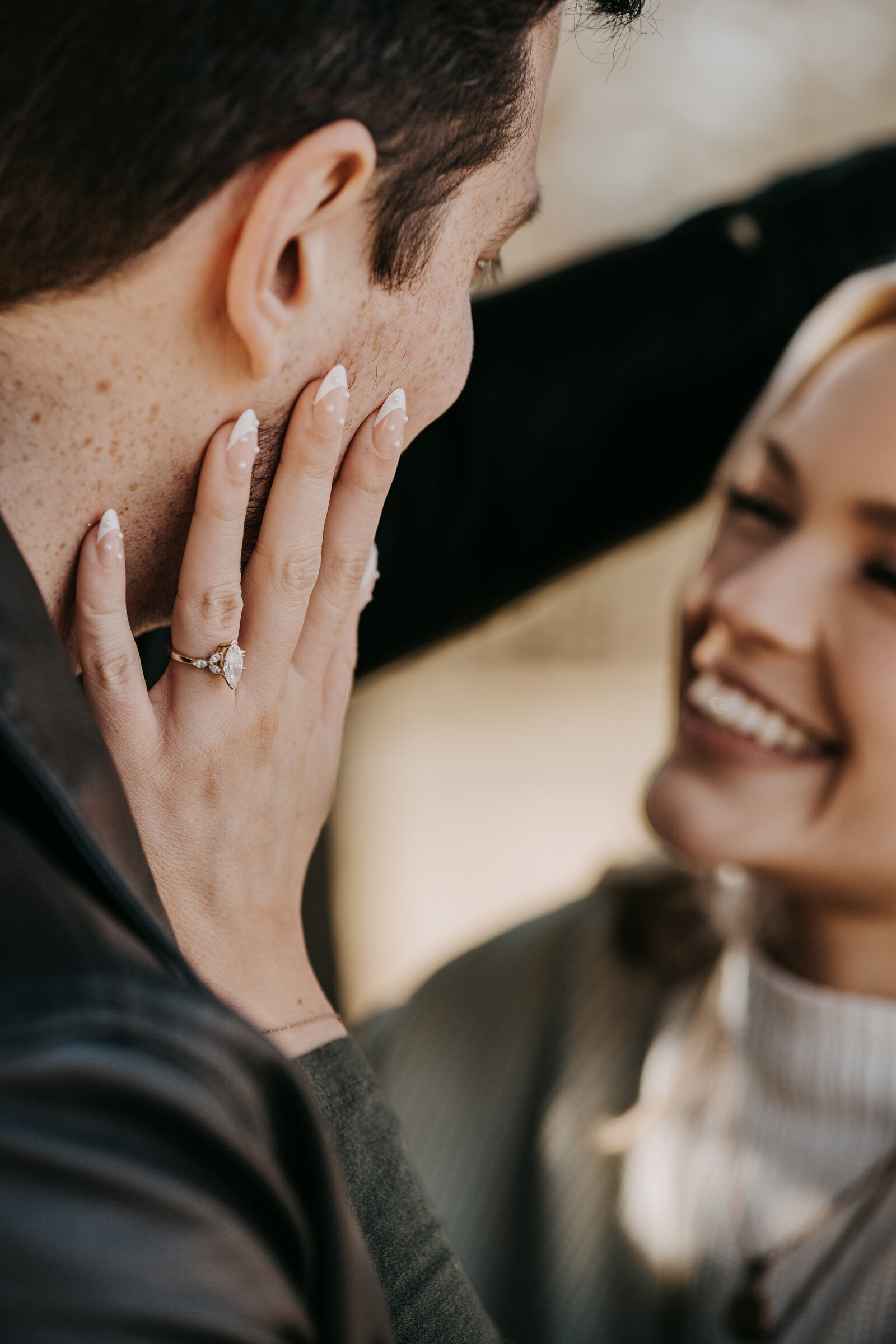 Rachel and Blaine smiling at each other, with her engagement ring in focus, capturing a joyful and intimate moment.