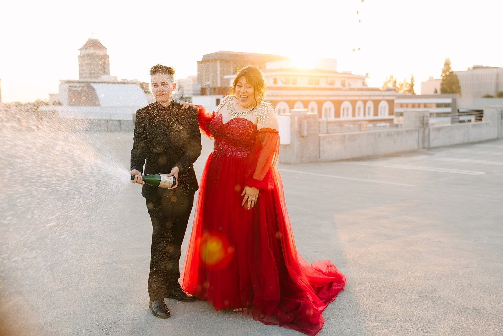 Two brides holding hands and laughing on the dance floor at their wedding, surrounded by friends and colorful motion blur lights, captured in a joyful, candid moment.