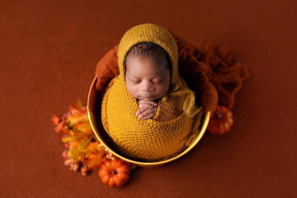Newborn baby boy in yellow wrap and bonnet fall themed bucket setup