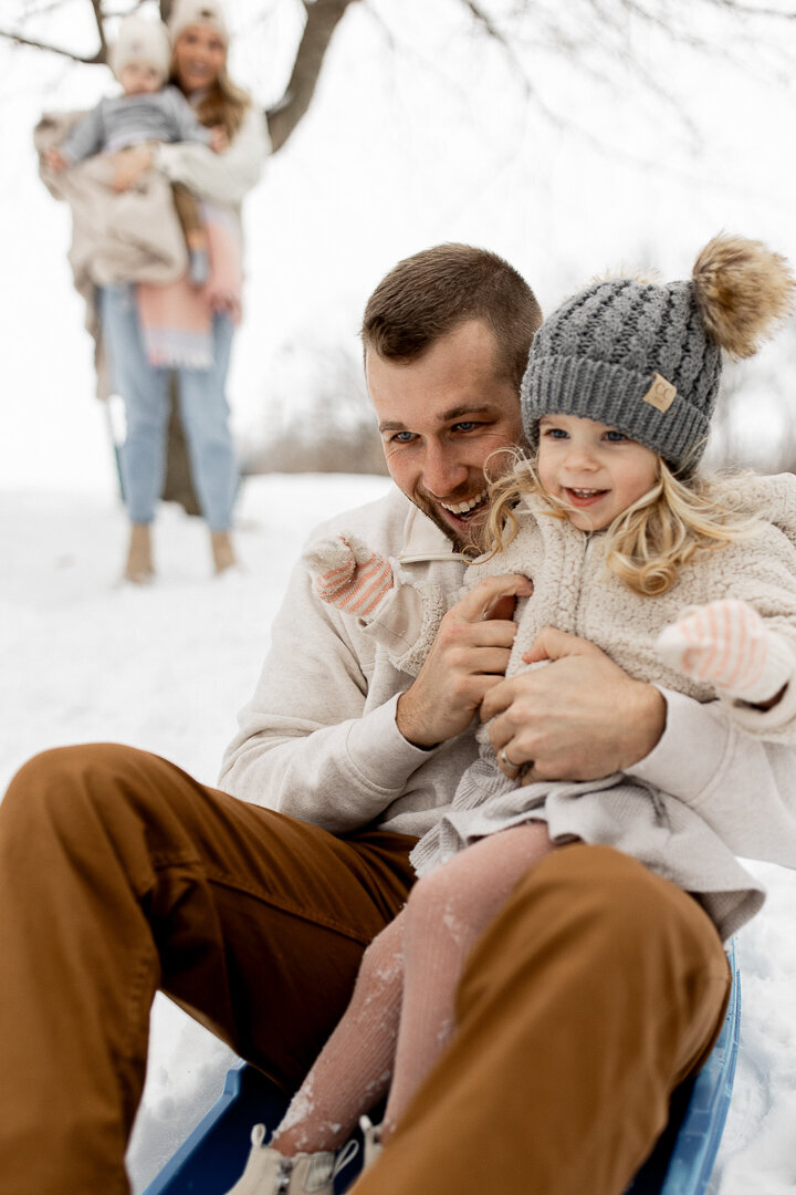 Des moines dad sledding with daughter while mother and son watch