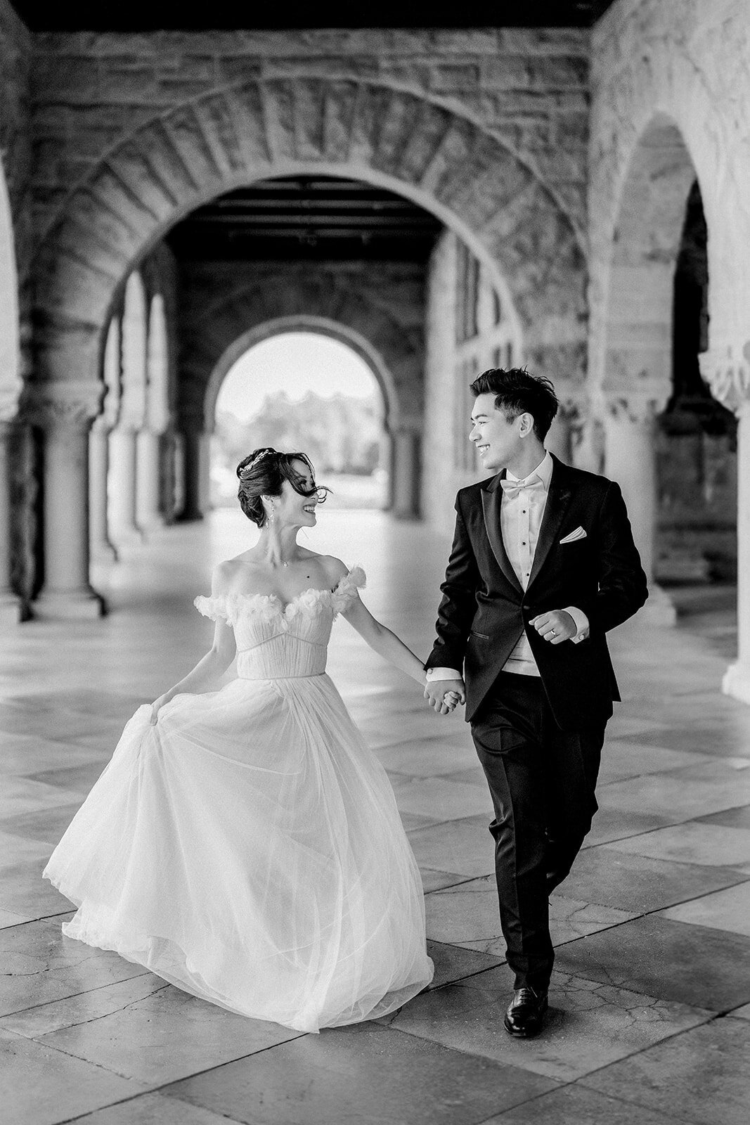 The bride and groom share a romantic moment under the archway at Stanford University, highlighting the venue’s classic beauty.