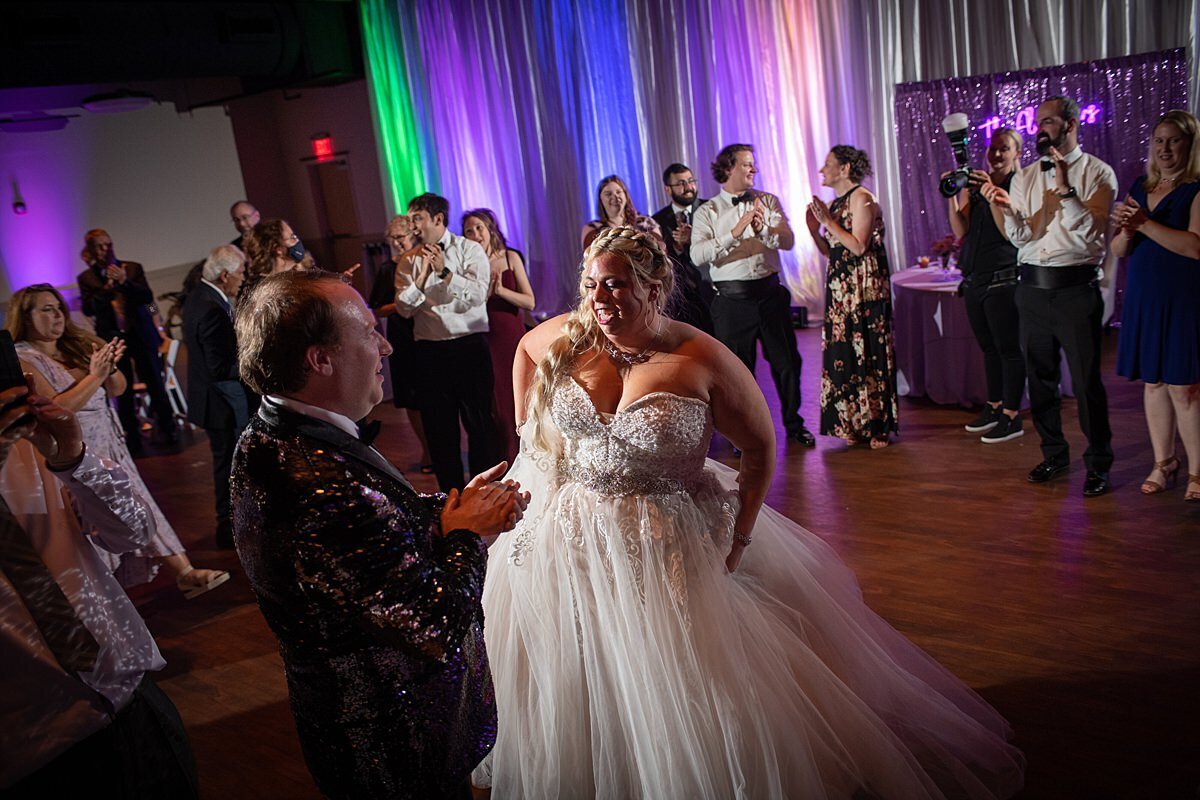 plus sized bride wearing a tulle wedding gown dances with the groom wearing a sequined tuxedo jacket