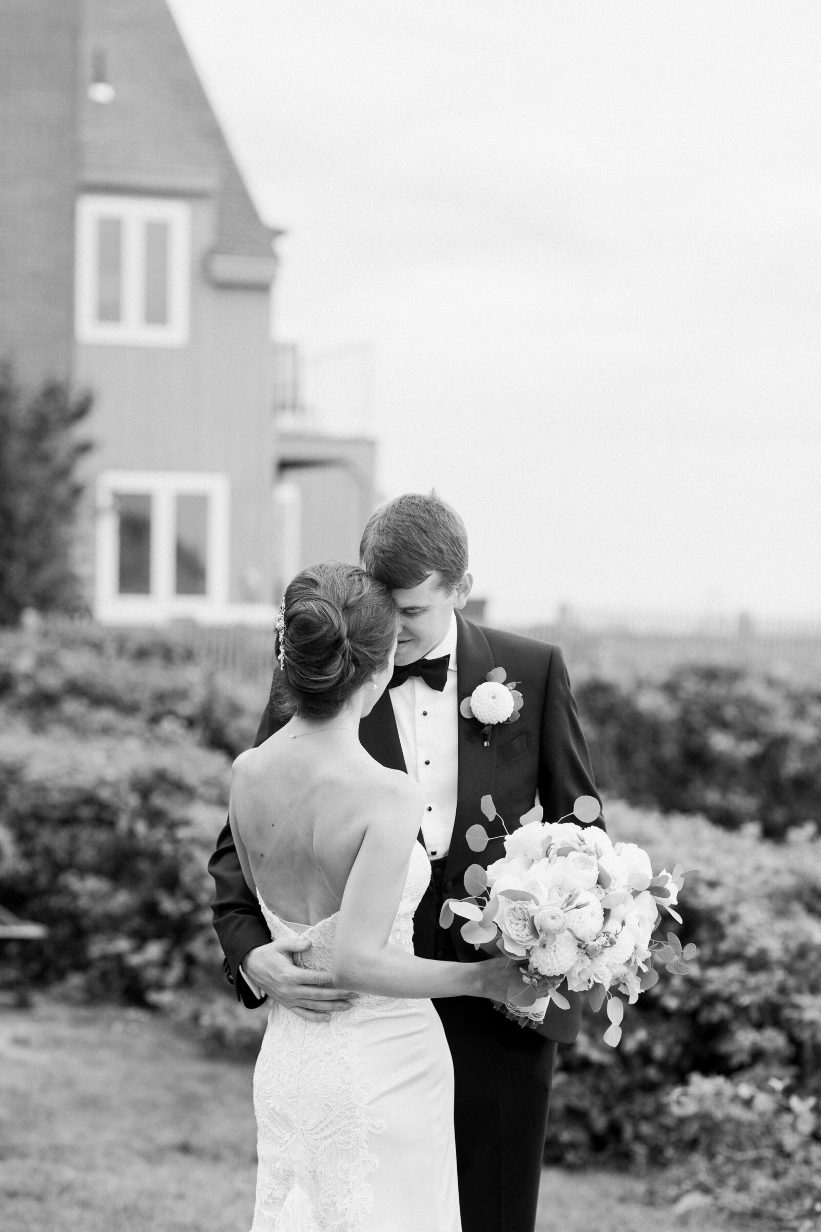 Wedding couple with their arms around each other and their foreheads touching.