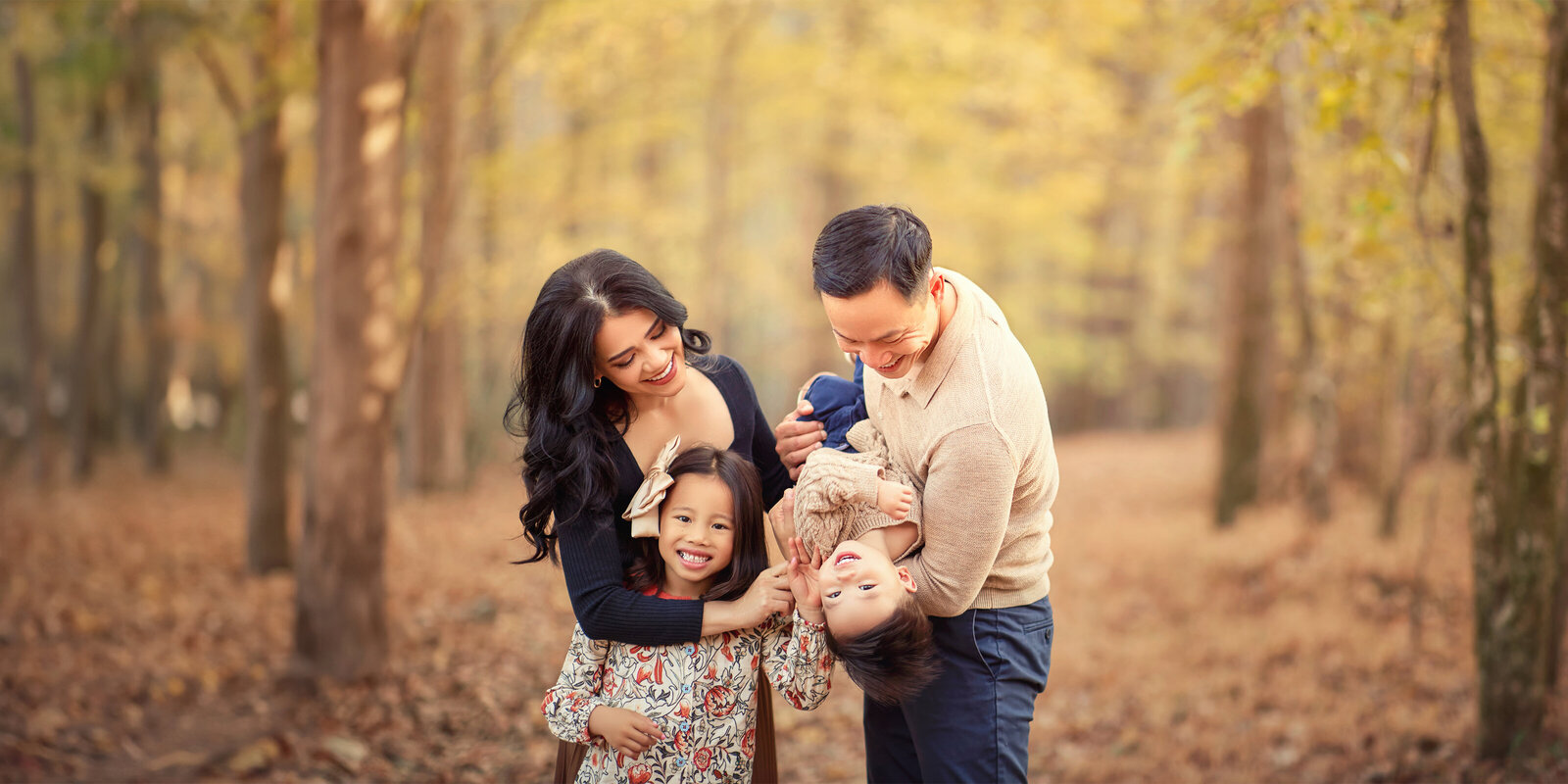 family with mother father daughter and son in the woods and forest in the fall tickling and laughing