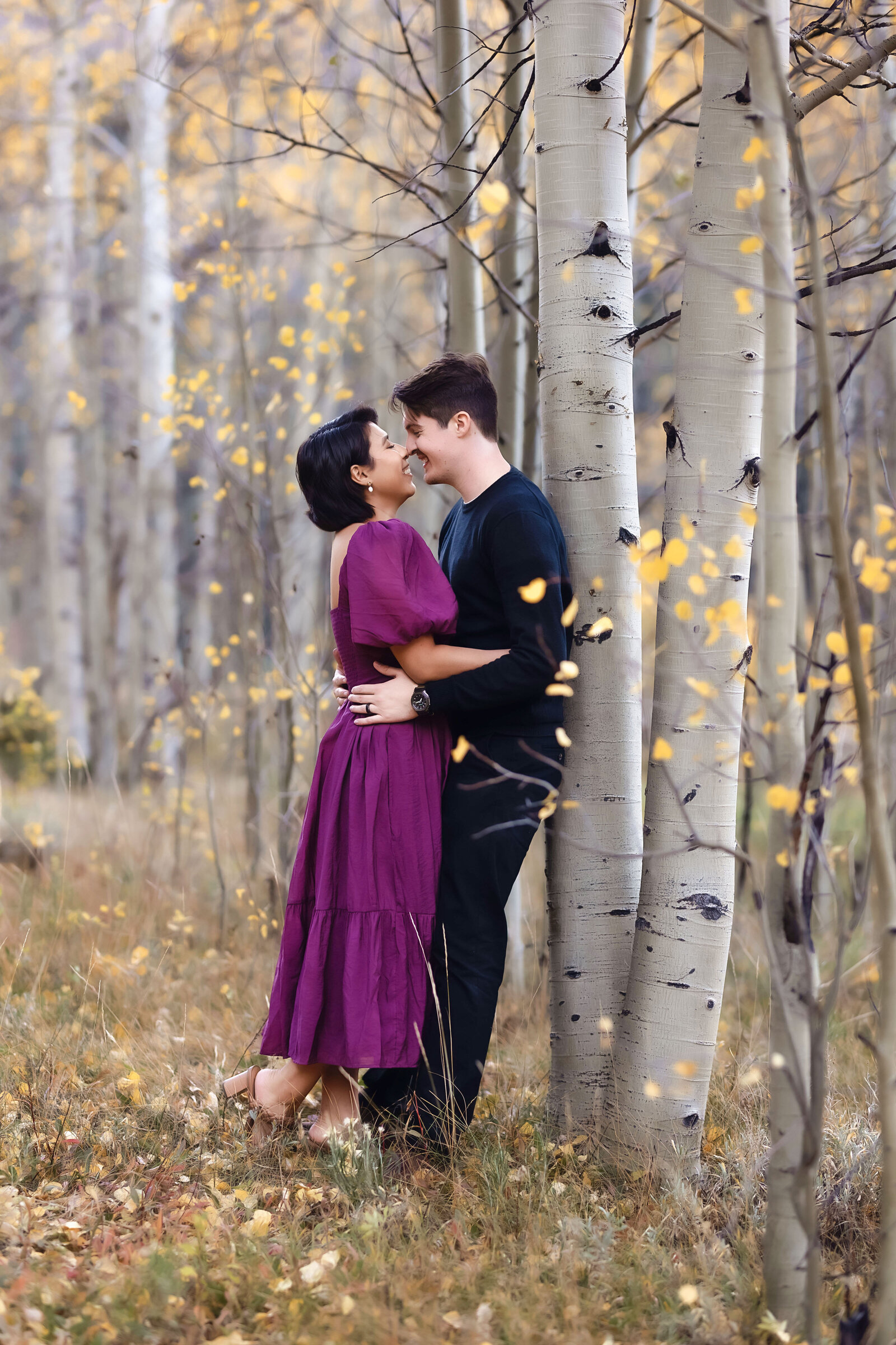 Beautiful woman in a bright purple dress kissed her fiance in an aspen grove, during their Aspen Engagement Photoshoot,