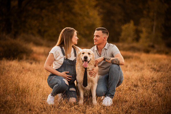 Een aanstaande moeder en haar partner poseren liefdevol met hun hond tijdens een zwangerschapsshoot, een intiem moment vol warmte en verwachting