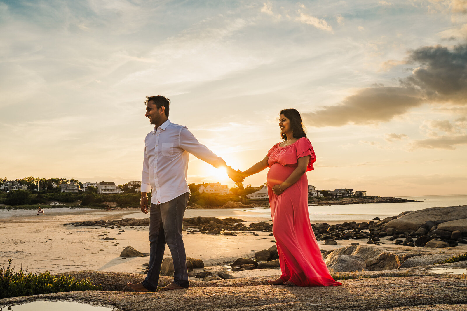 man guides pregnant wife over ocean rocks