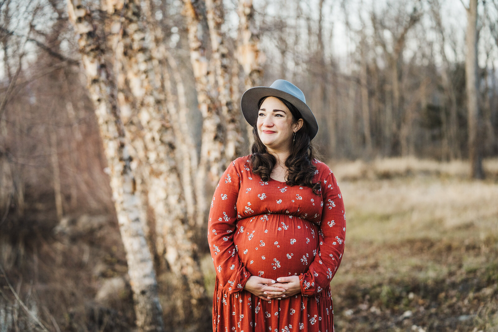 pregnant woman in red dress stands in front of birch trees
