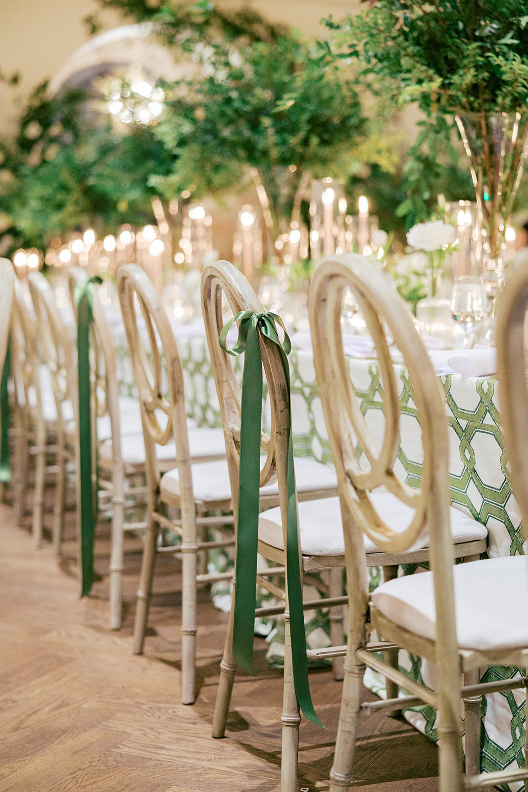 tan chairs with green bow ribbon and patterned table cloths with greenery in urns