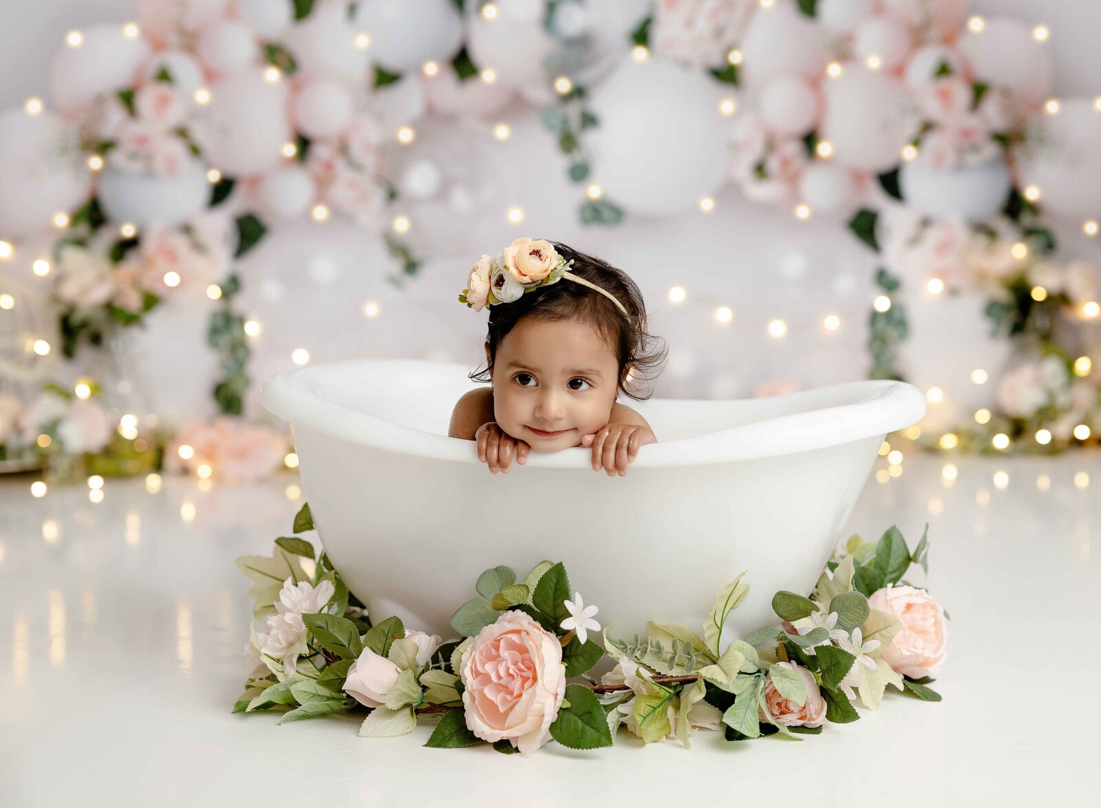 Baby girl leaning on floral tub with her hands under chin. Photographed by Jenni Nikki at Atlanta photo studio.