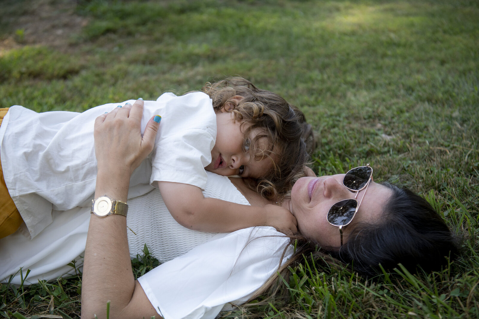 A parent laying down in the grass with their child laying on top of them 