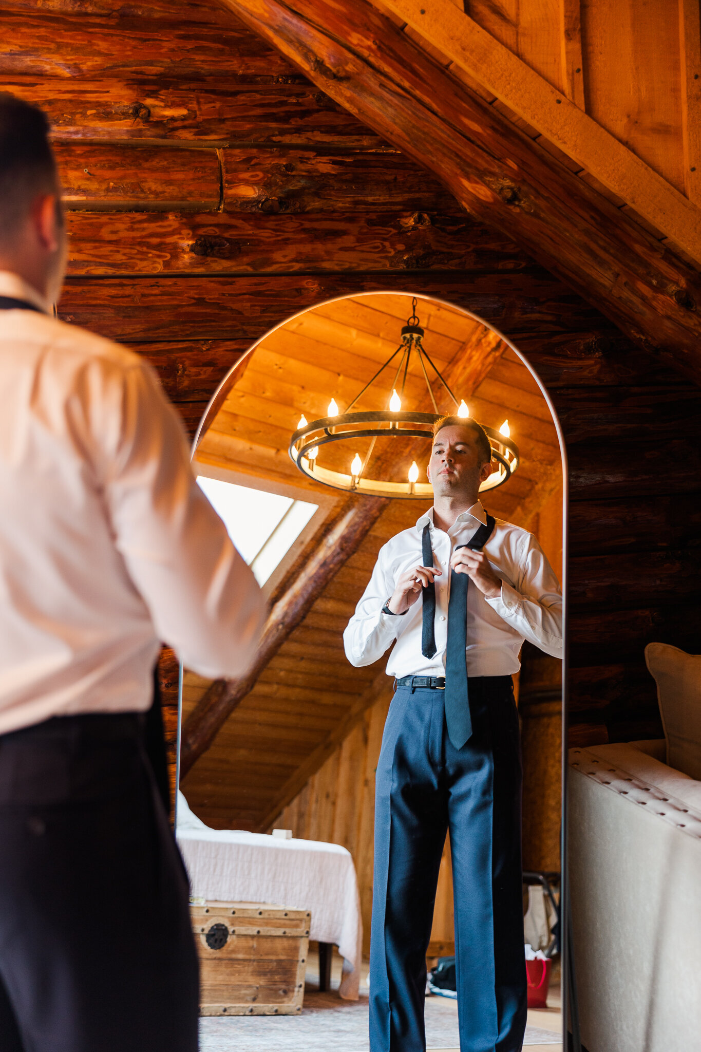 Groom looking into mirror while adjusting tie on wedding day at SkyView Golf Club in Sparta

