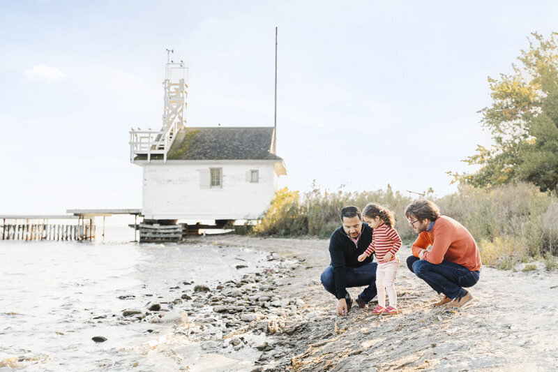 2 dads and their daughter looking at rocks to throw into the water at Cherry Beach, toronto