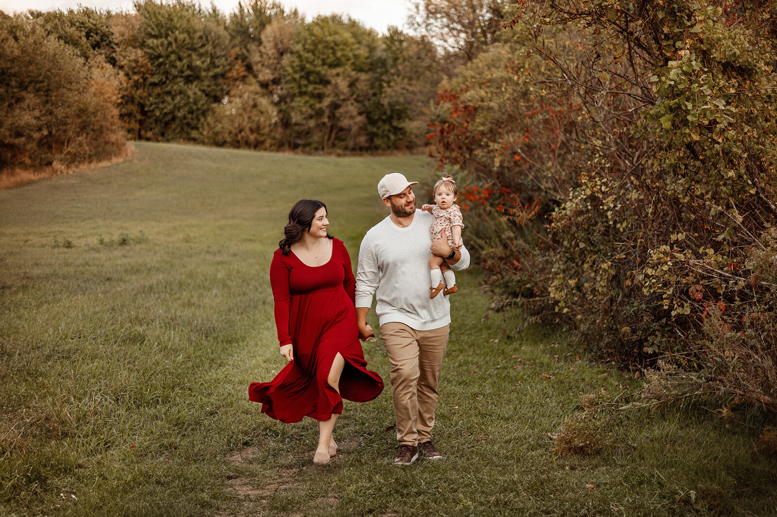 A family of three walking through a scenic grassy field in Grand Rapids, Michigan, during a golden-hour family photography session, capturing natural and joyful moment
