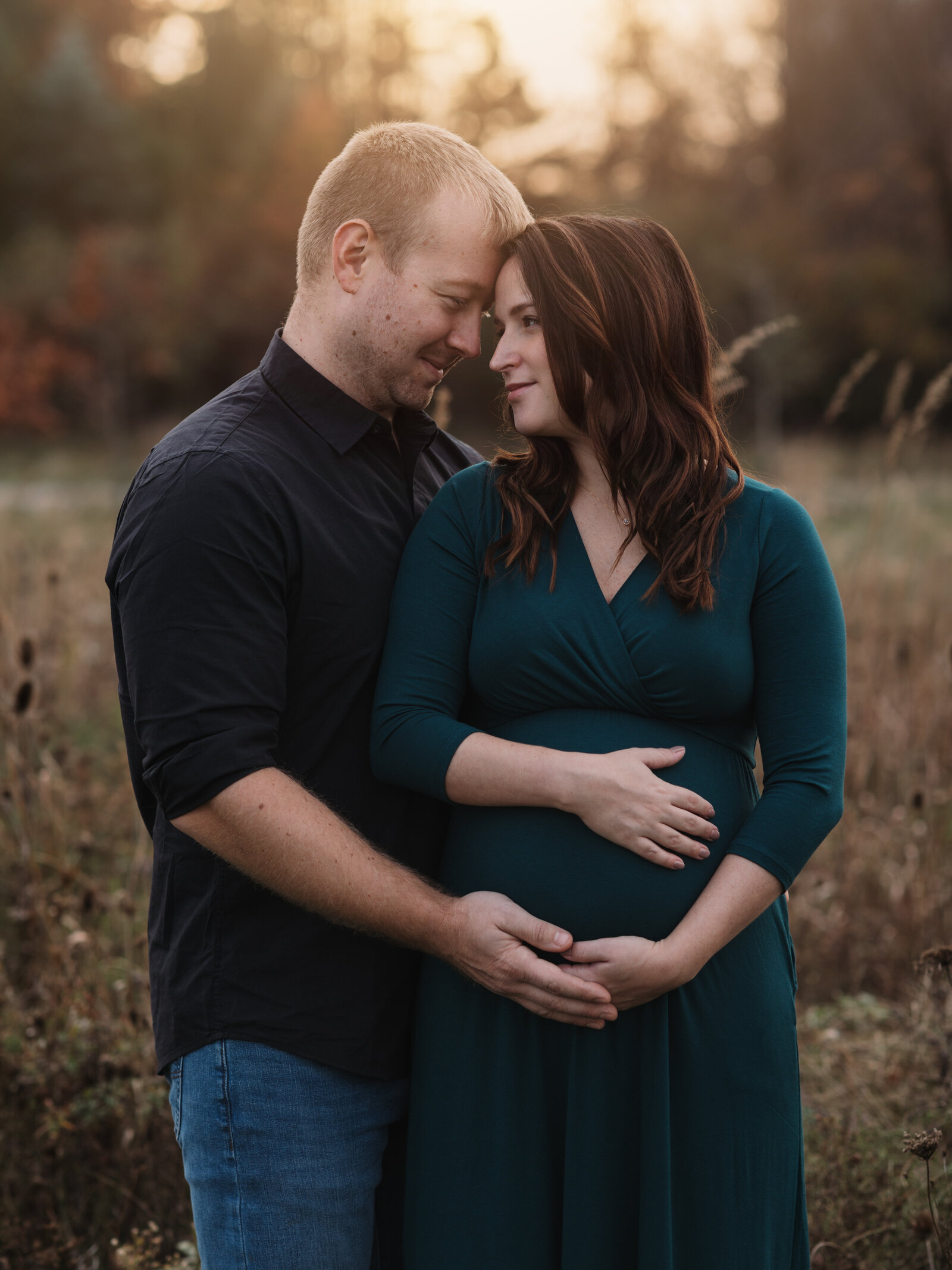 husband and pregnant wife in green dress posing for maternity photos at park