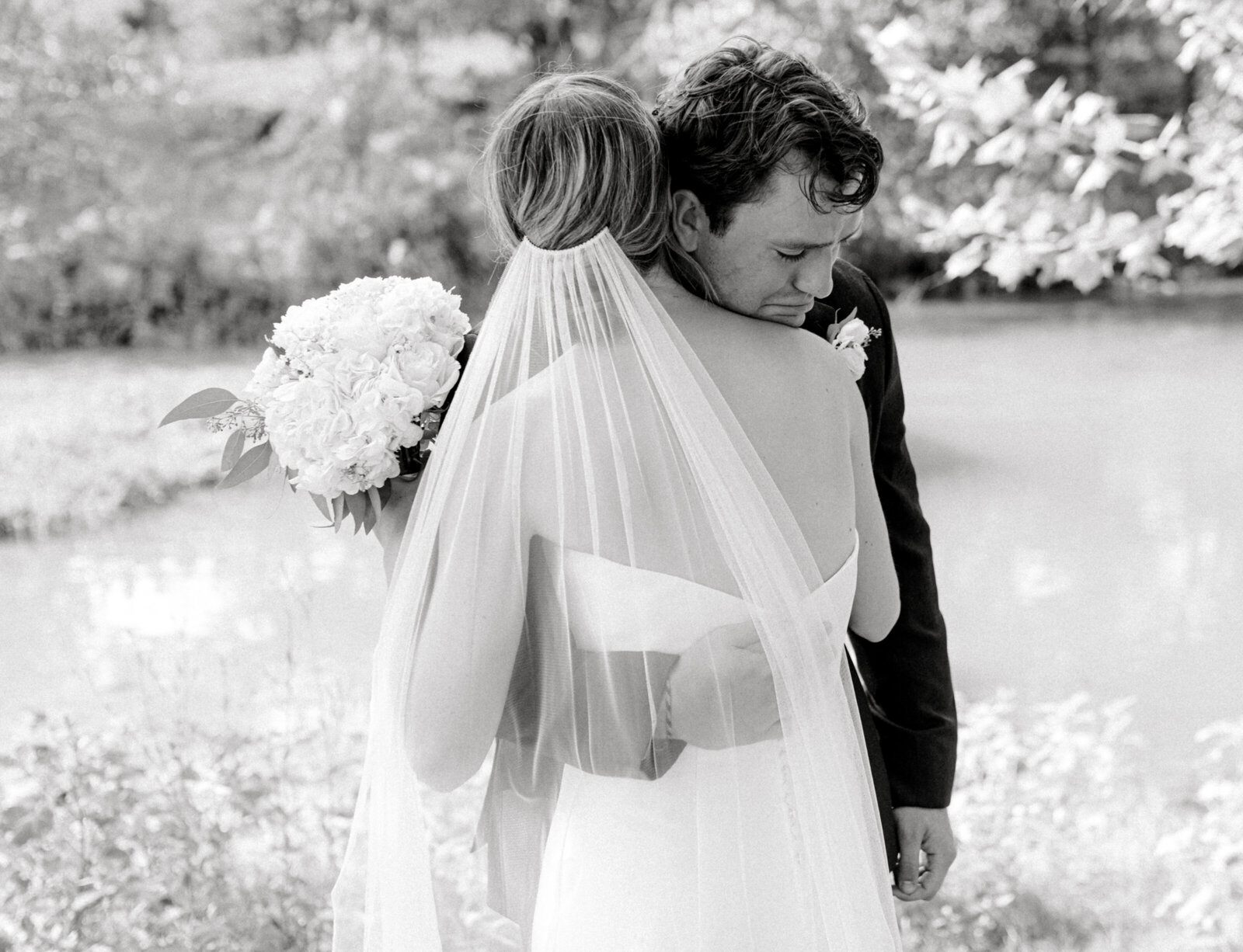 Black and white image of groom crying hugging bride