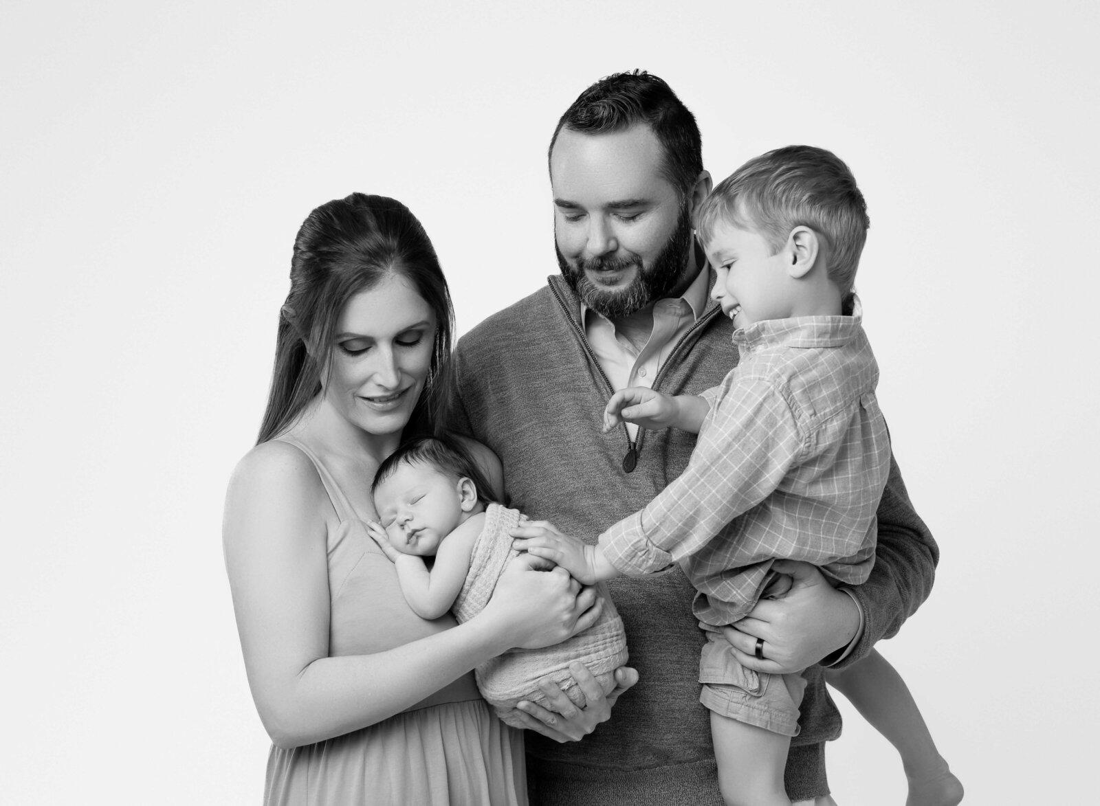 Family of 4 looking at newborn baby boy and sibling touching baby's back.